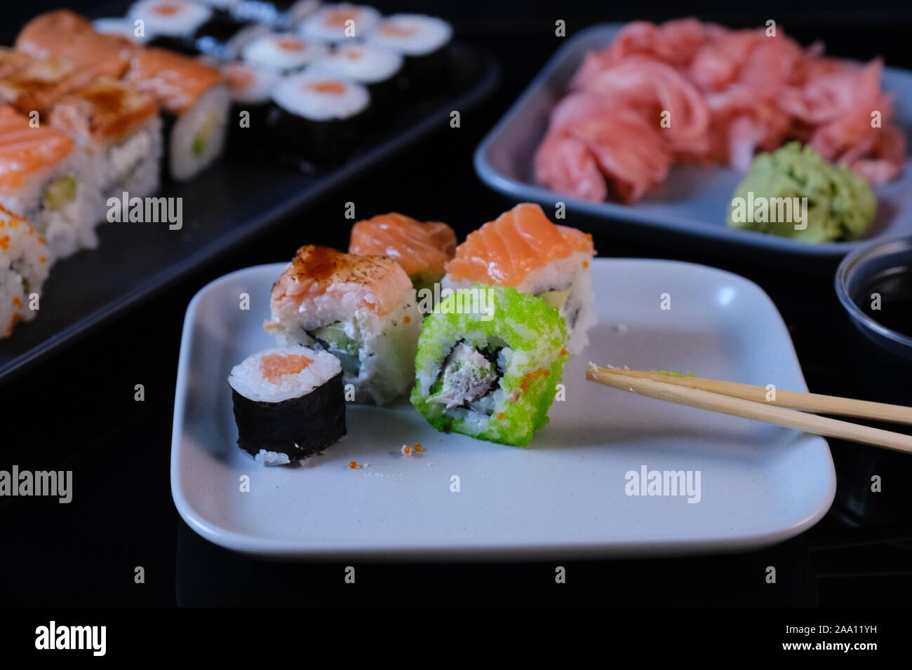 Rotolo di Sushi con salmone e pesci volanti caviale su una tavola nera. Rotolo di Sushi con piatti a base di frutti di mare e salsa di soia, wasabi e zenzero. Foto Stock