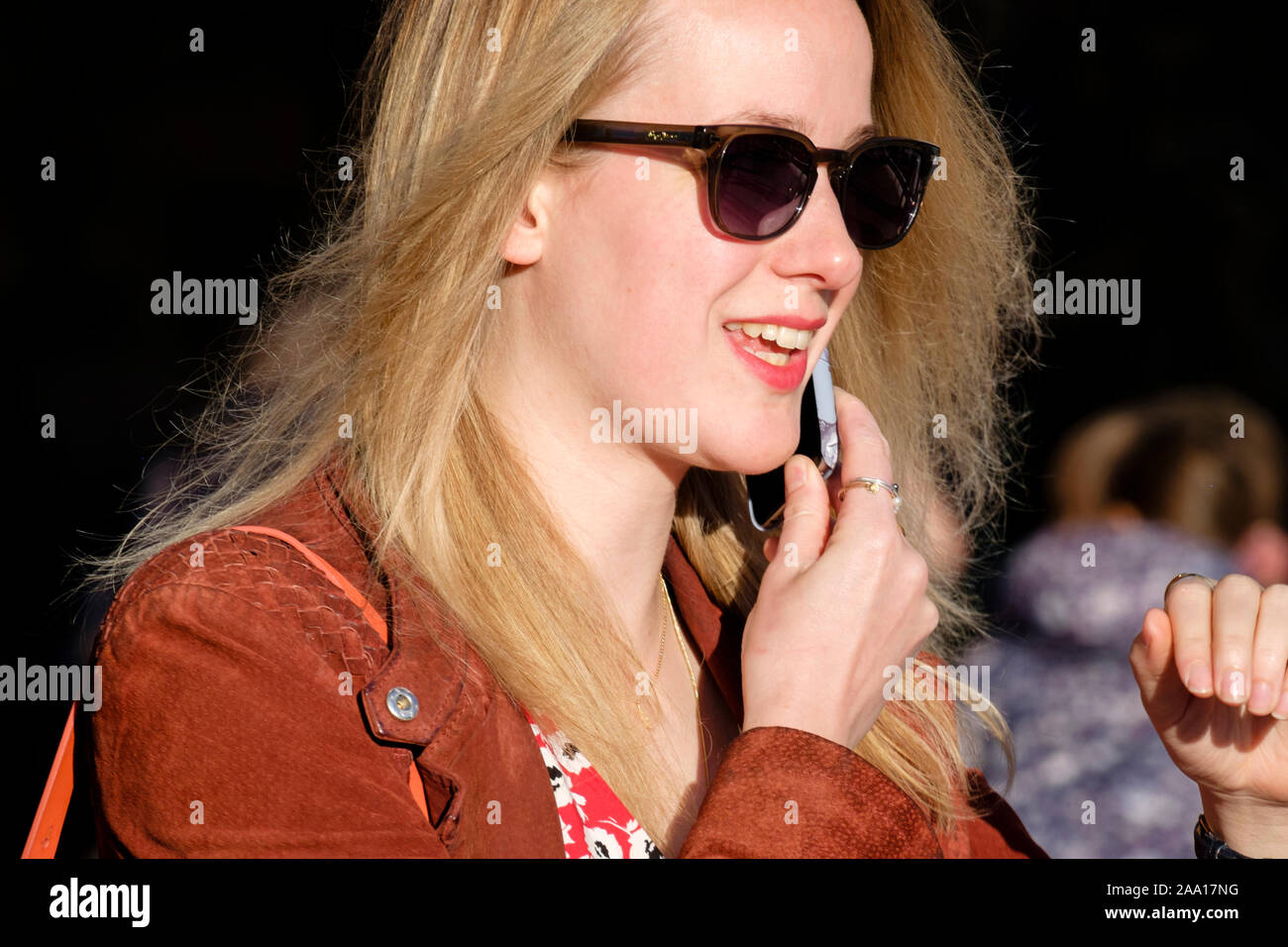 Donna, 20 anni, capelli biondi, abito casual alla moda, occhiali da sole, con il telefono cellulare, sorridendo. Foto Stock