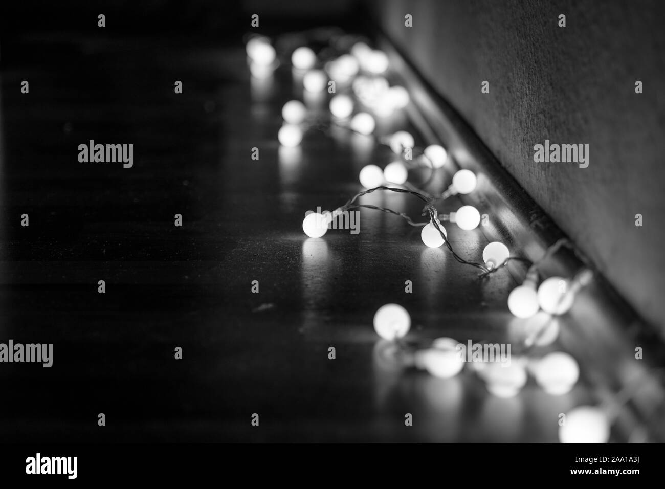 Bianco e nero umore e il tono della vista ravvicinata del filo decorativi piccoli led a luce bianca calda lampadine giacciono su un piano ad angolo del buio e camera dim. Foto Stock