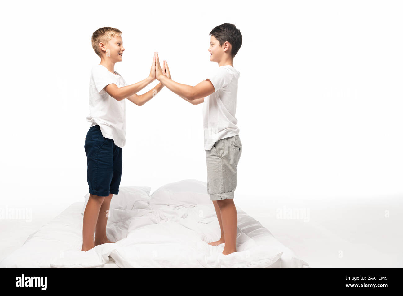 Due fratelli sorridente battendo le mani mentre si sta in piedi sul letto isolato su bianco Foto Stock