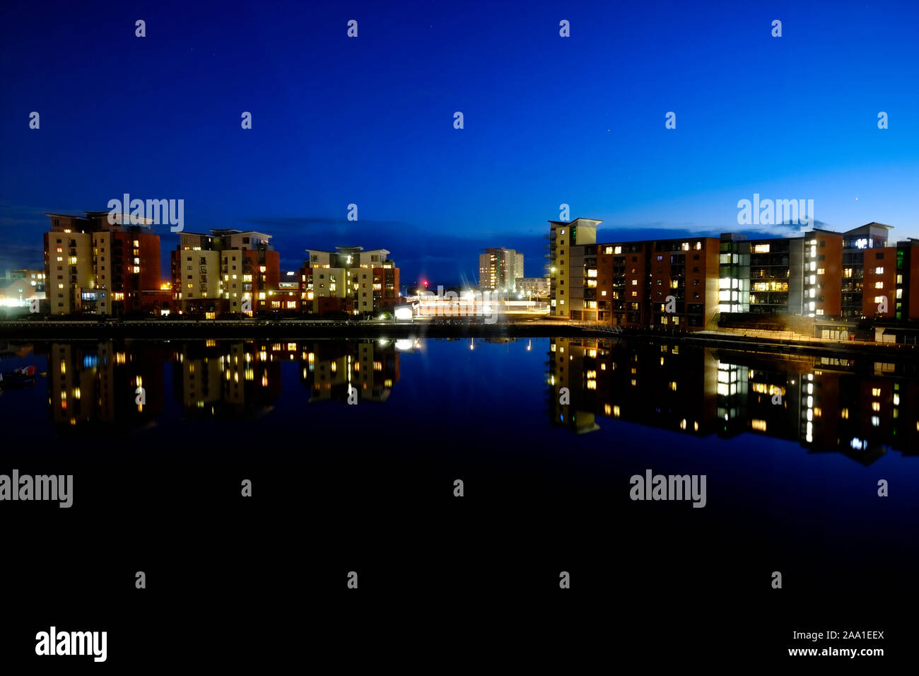 Swansea Docks e Marina al crepuscolo cercando in tutta l'acqua a lit fino ad alto luogo di blocchi di abitazioni appartamento riflettendo sull'ancora la superficie dell'acqua Foto Stock