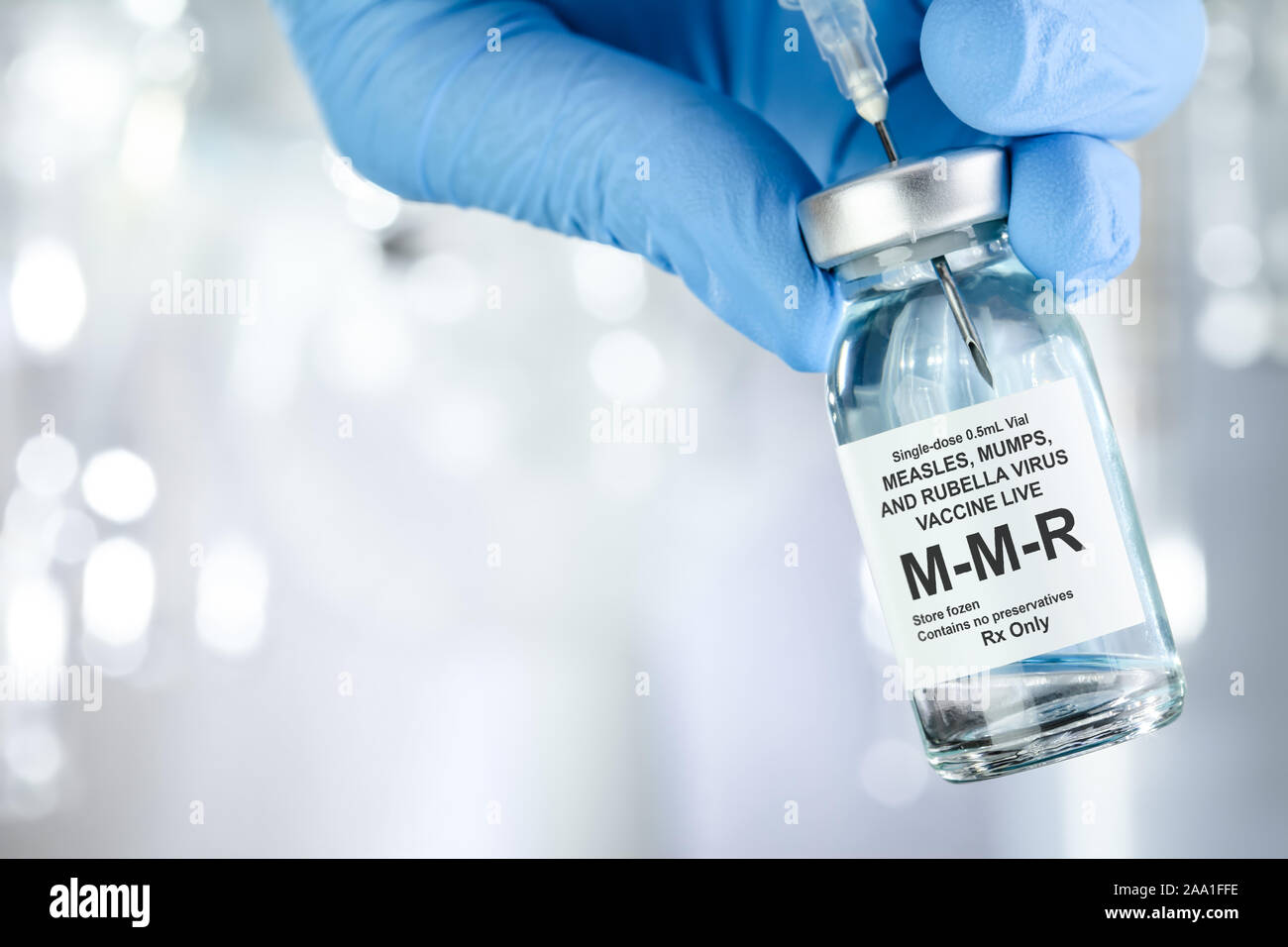 Il concetto di assistenza sanitaria con una mano in blu guanti medicali azienda MMR, morbillo, parotite e rosolia, flaconcino di vaccino Foto Stock