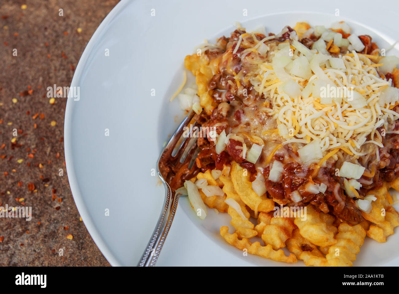 Ciotola bianco pieno di golden patatine fritte soffocato in casalingo di peperoncino e sormontato messicano con il formaggio e la cipolla tritata Foto Stock