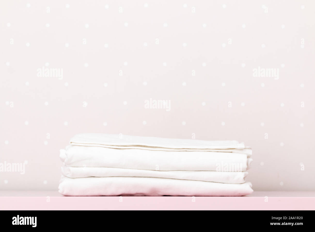 Primo piano di una pila di pulire biancheria da letto bianca su una tabella da una parete di luce. Copia dello spazio. Foto Stock