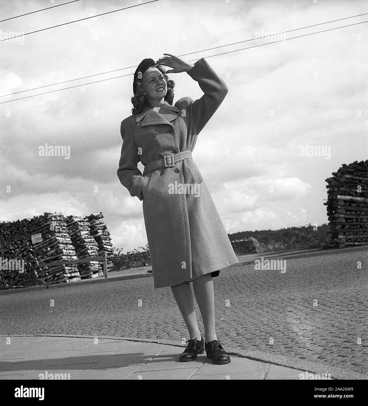 Le donne della moda nel 1940s. Una giovane donna in un tipico degli anni quaranta cappotto. È il dopoguerra in Svezia e non vi è ancora una mancanza di combustibile e carbone per il riscaldamento e le cataste di legna da ardere è visibile in background. Kristoffersson Ref V78-2. La Svezia 1947 Foto Stock