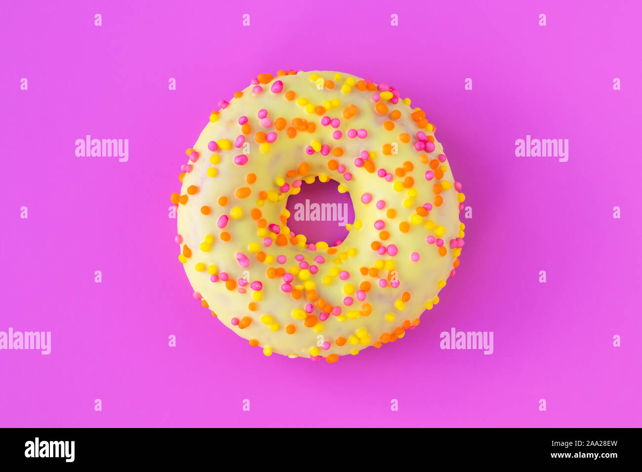 Vetrata ciambella gialla con multicolore spruzza sul rosa luminoso dello sfondo. Malsana alto-caloria cibo. Divertente il concetto dell'umore. Laconico il food design. Foto Stock