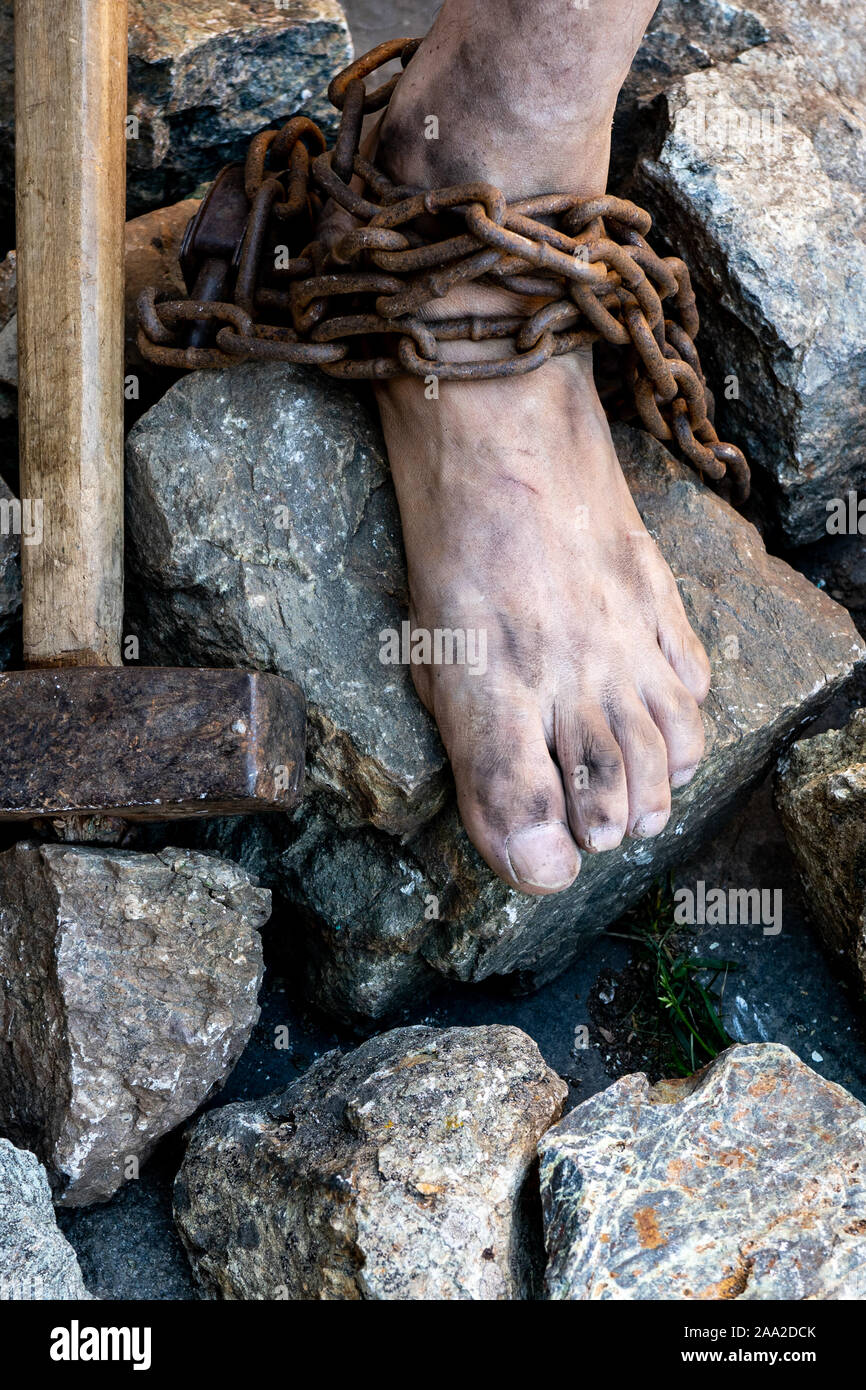 Sporco gambe slave in catene tra i sassi. Slave nel tentativo di liberarsi. Il simbolo della schiavitù. Foto Stock