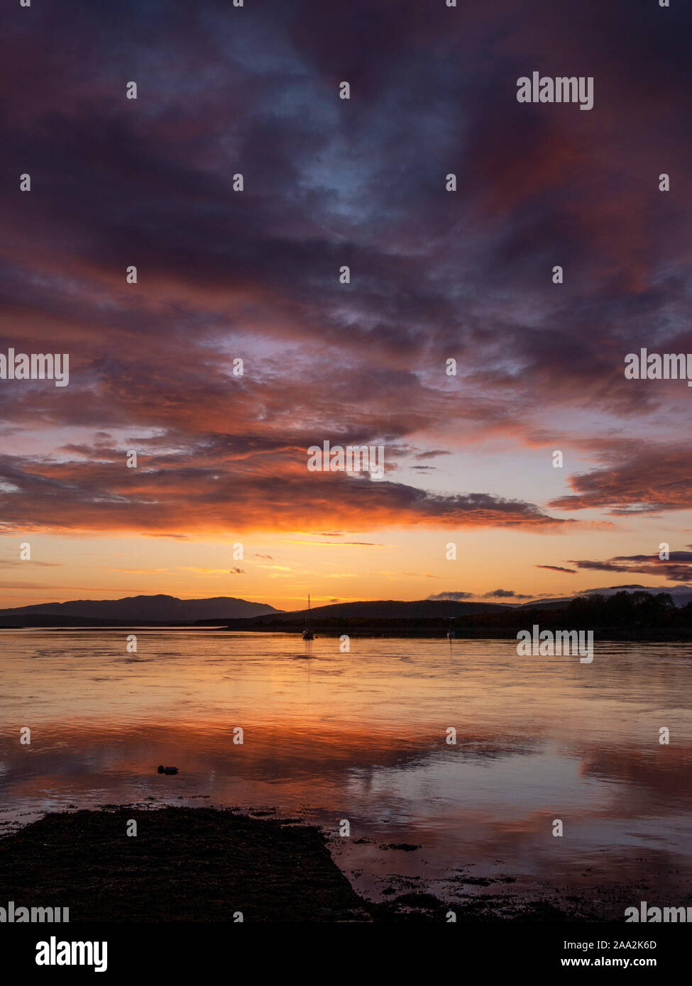 Rosso infuocato, rosa, viola e arancione tramonto riflesso nella calma, ancora la presenza di acqua in corrispondenza della bocca del Loch Etive, Connel, Oban, Argyll and Bute, Scotland, Regno Unito Foto Stock