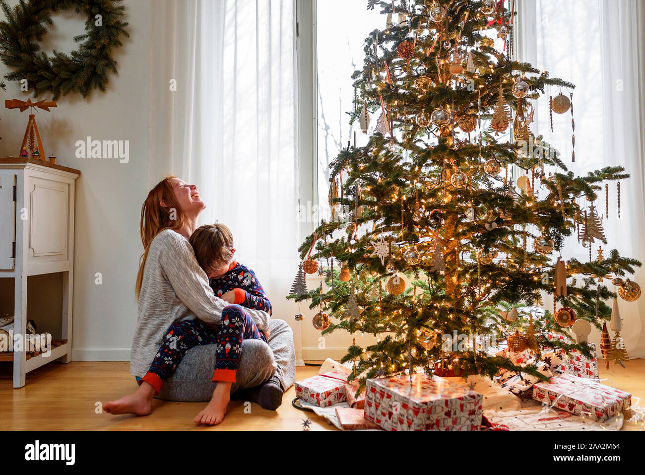 Madre e figlio giovane cuddling accanto a un albero di Natale Foto Stock