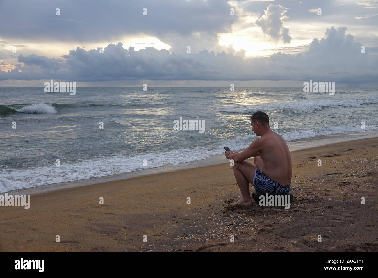 Giovane con telefono cellulare sull'oceano tropicale spiaggia al tramonto Foto Stock