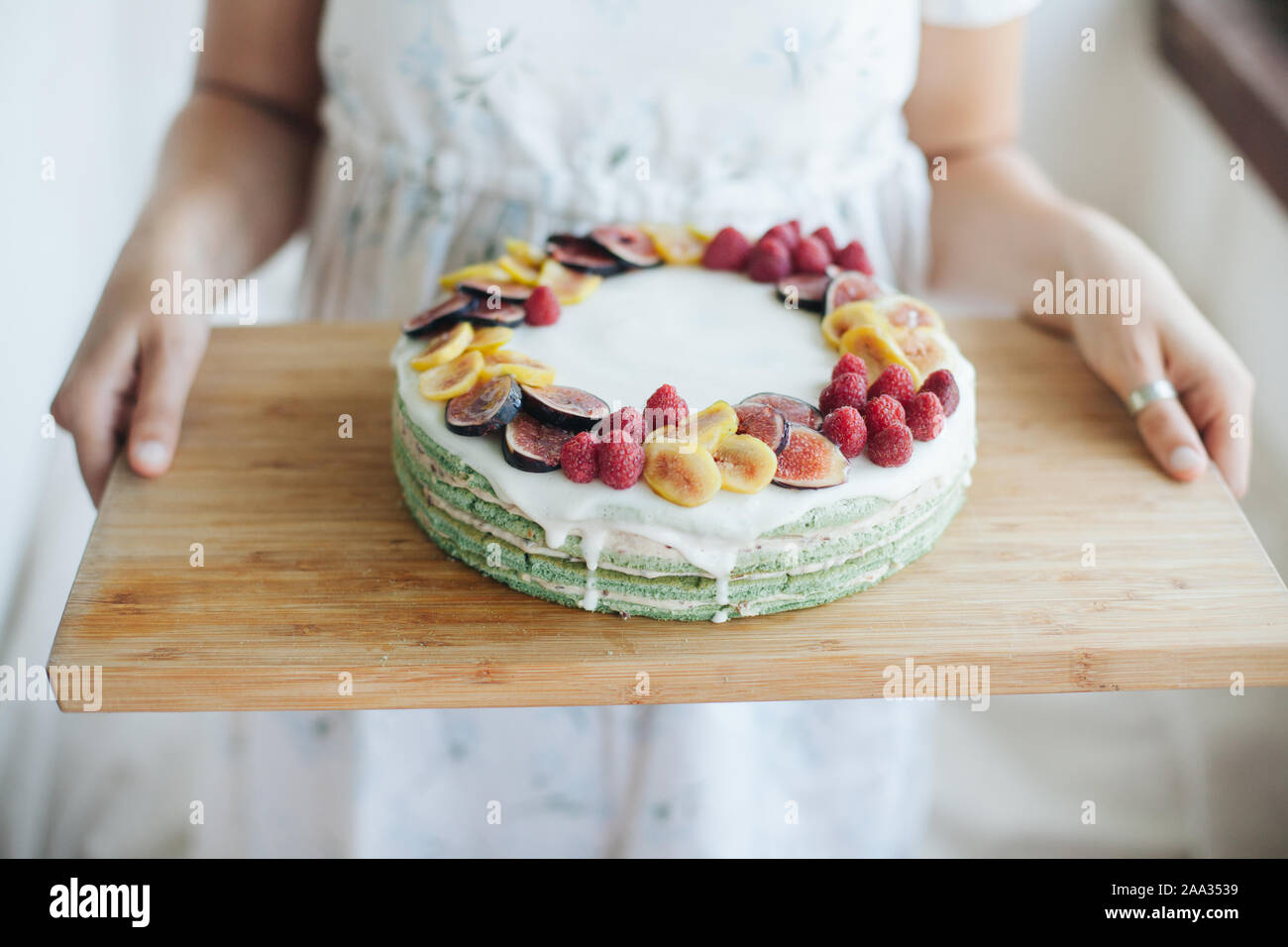 Donna che la porta in casa la torta con fichi e lamponi su un tagliere di legno Foto Stock