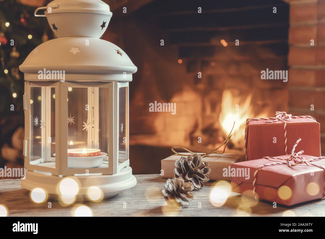 Lanterna con una candela che brucia, doni su una tavola di legno in una stanza con un albero di Natale e un caminetto per la Vigilia di Natale. Foto Stock