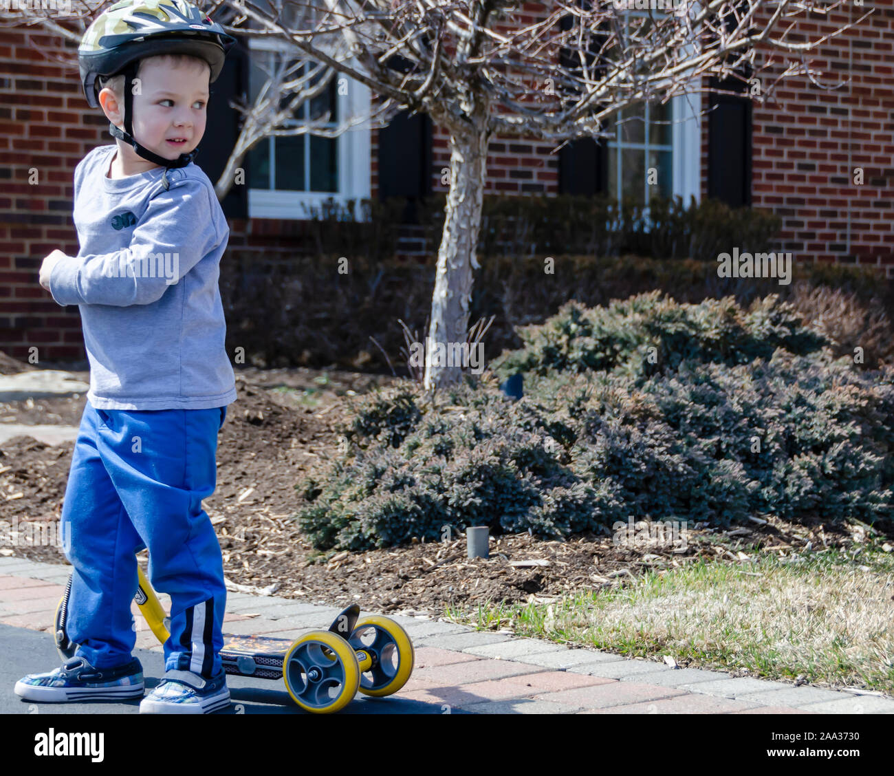 Un giovane ragazzo che indossa un casco e in piedi accanto ai suoi tre ruote di kick scooter. Foto Stock