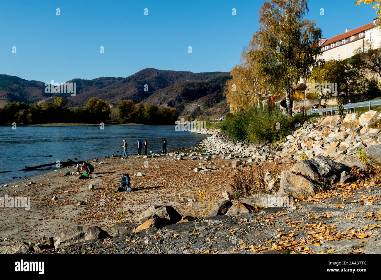 La gente sul lungofiume, godendo di una vista mozzafiato sul fiume Danubio a Durnstein, con le montagne sullo sfondo Foto Stock