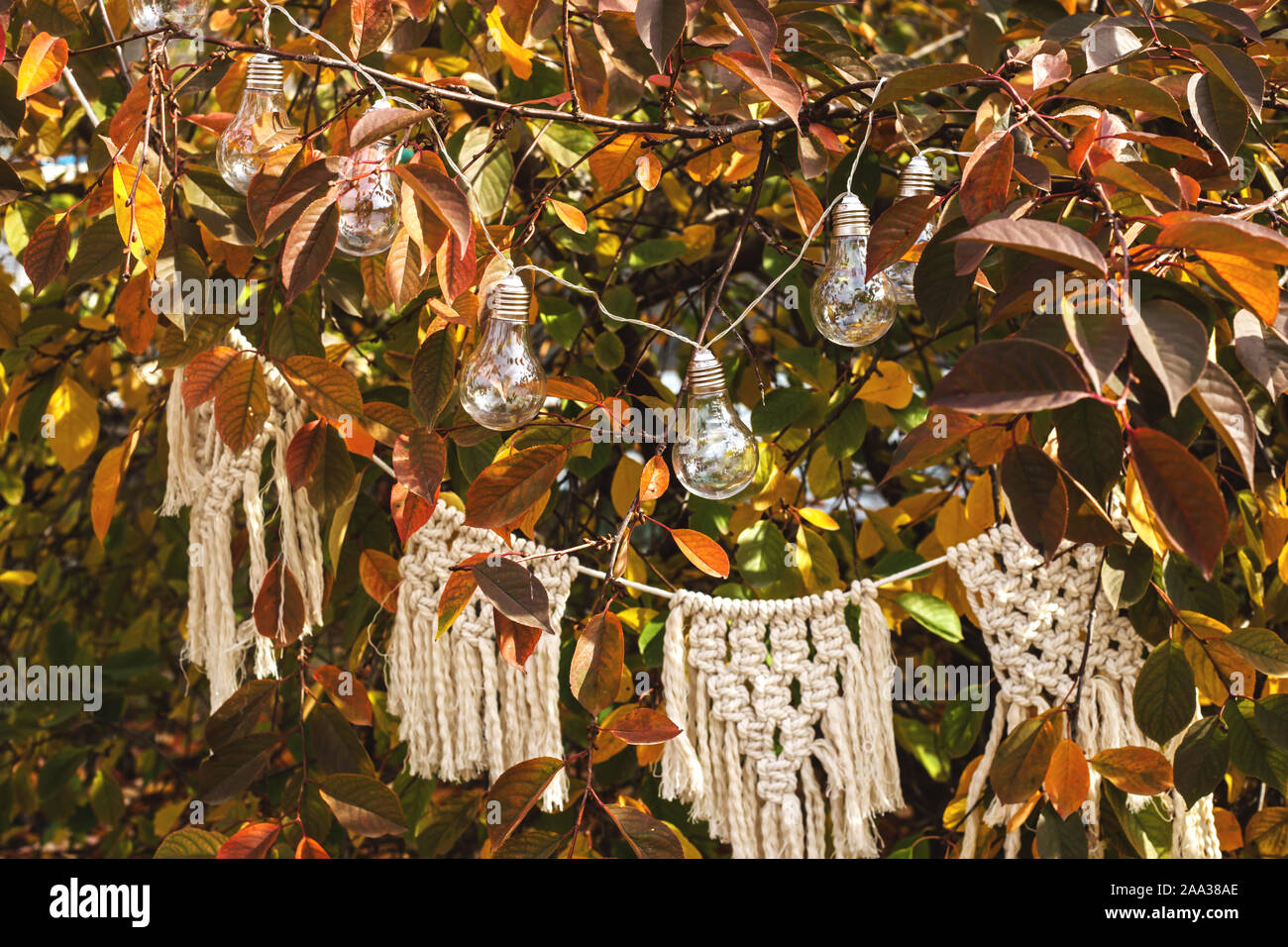 Arredamento per un autunno la cena in un giardino su un albero di colore giallo con bulbi luminosi e un cotone bianco macrame garland in stile Boho. Foto Stock