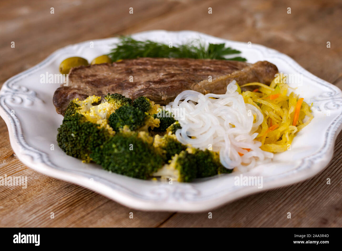 Grigliate di carni cucinate fresche, broccoli, vegetale spaghetti shirataki, il ravanello di daikon insalata, olive. Paleo e cheto dieta piatto. Rustico vista sullo sfondo. Sele Foto Stock