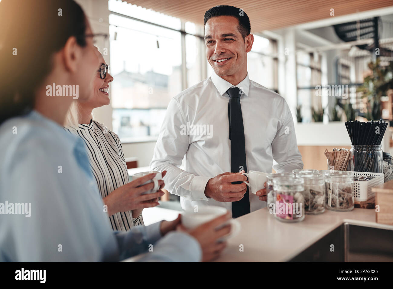 Gruppo di sorridere i giovani imprenditori chiacchierando tra loro durante la pausa caffè in un luminoso ufficio moderno Foto Stock