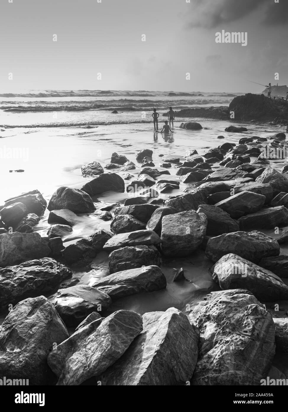 Bambini che giocano in Goa seashore con rocce e mare in bianco e nero Foto Stock
