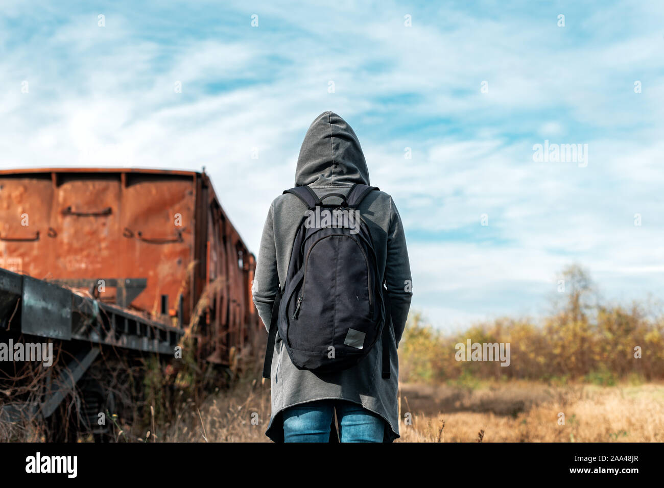 Donna senzatetto con zaino allontanarsi da tutto e da tutti, vista posteriore delle donne in cammino tra abbandonato i vagoni del treno e ferrovia obsoleti via Foto Stock