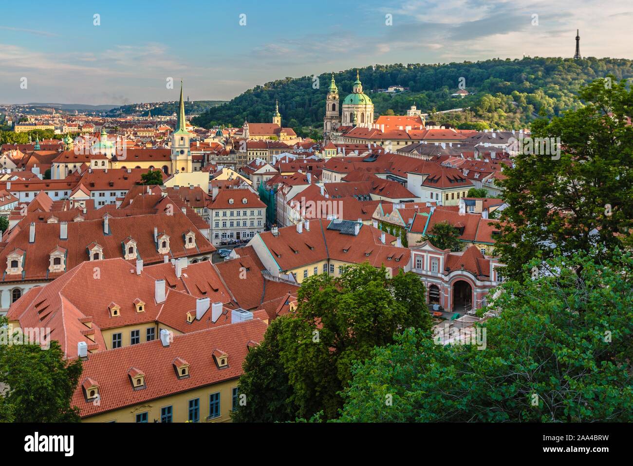 Praga, Repubblica Ceca - 20 Luglio 2019: vista dei tetti rossi, paesaggio urbano con chiese e distante Petrin Hill con una torre. Il blu del cielo della sera con nuvole. Foto Stock