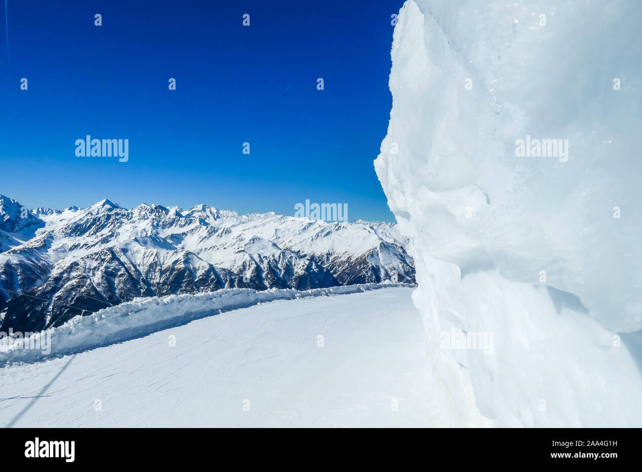 Lato congelate di Boulder. Parete ghiacciata impedisce gli sciatori da sbattere contro una roccia. Perfettamente battute pendenza con una vista su alti, neve-Alpi tappata. Sunny d Foto Stock