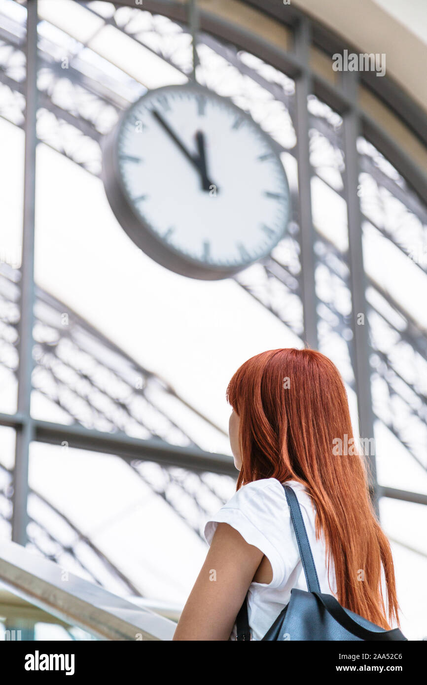 La donna si erge su sfondo sfocato di orologio da parete Foto Stock