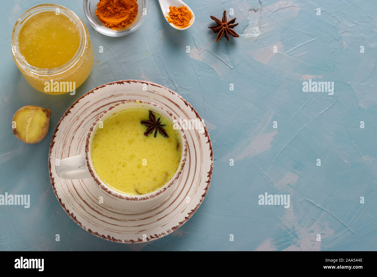 Tazza di ayurvedic golden curcuma latte latte con curcuma in polvere, la cannella, lo zenzero e anice stella su fondo azzurro, vista dall'alto Foto Stock