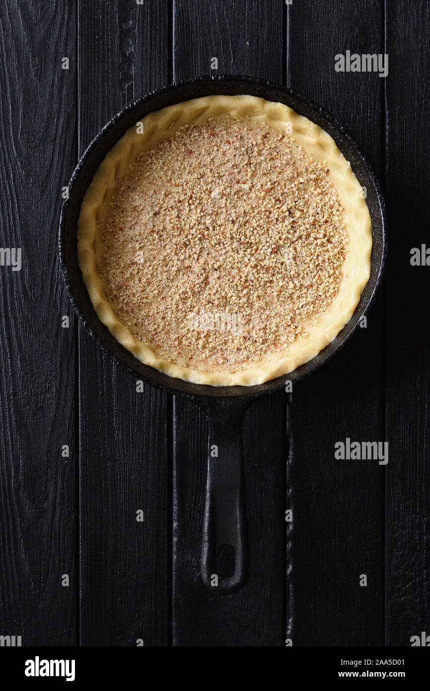 La pasta frolla. Materie crosta con mandorle tritate per aprire la torta in ghisa pan su sfondo nero in vista superiore spazio copia vista aerea Foto Stock