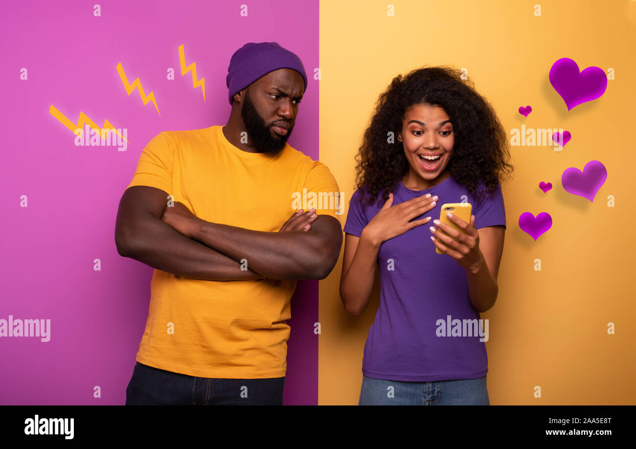 Ragazza ricevere un sacco di focolari sul sociale e del ragazzo è geloso su di esso. Giallo e viola sullo sfondo Foto Stock