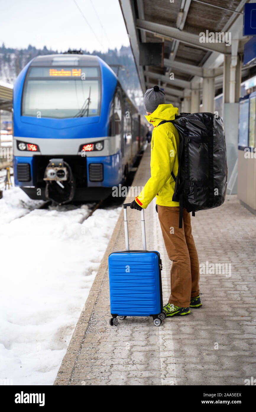 Per turisti in cerca di fotocamera con valigia blu alla stazione in attesa del treno contro sullo sfondo di montagne sulla giornata invernale Foto Stock