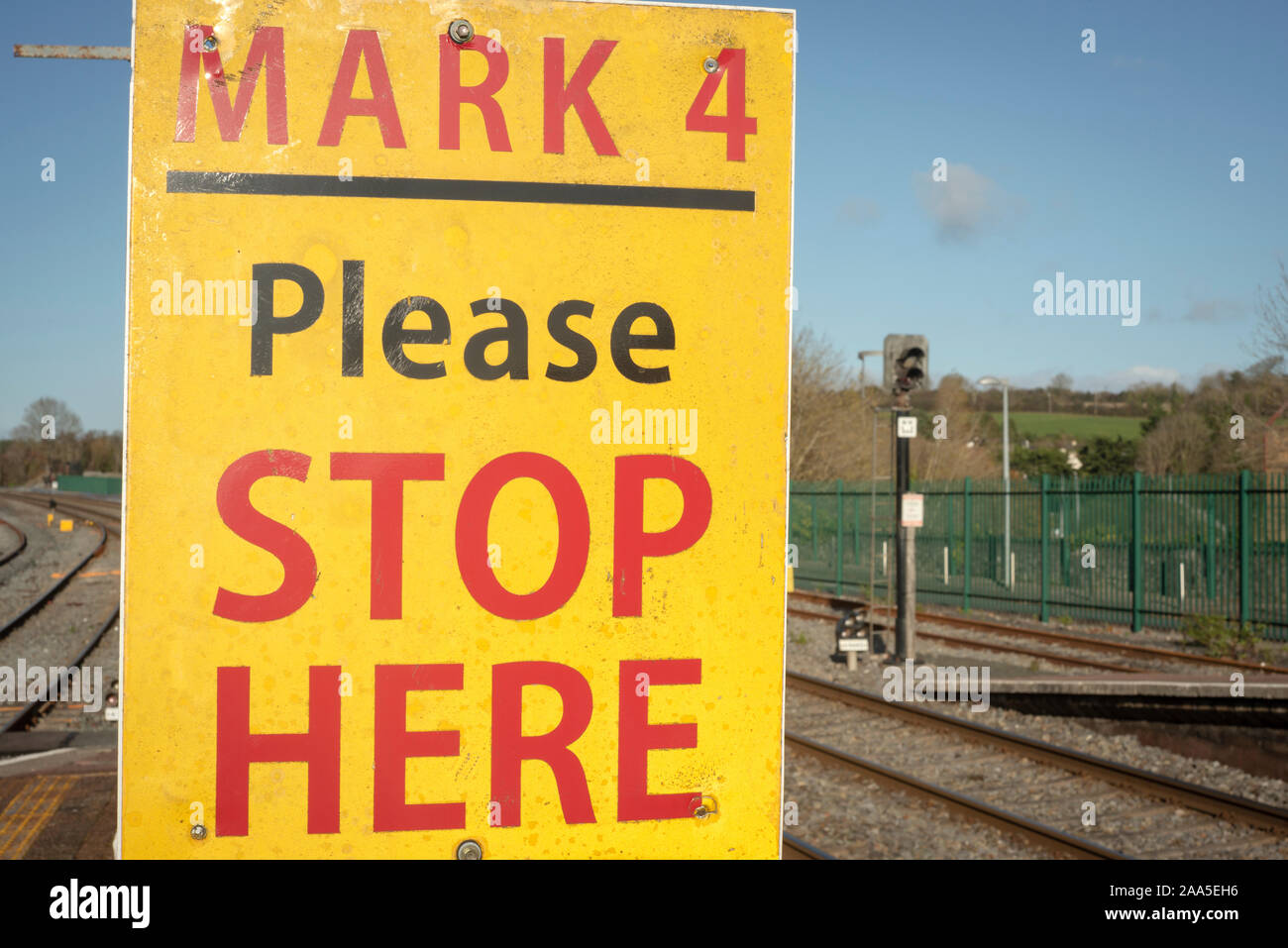 Si prega di interrompere qui cartello giallo alla stazione ferroviaria o stazione ferroviaria piattaforma in Irlanda come un avvertimento a non attraversare la via linee. Foto Stock