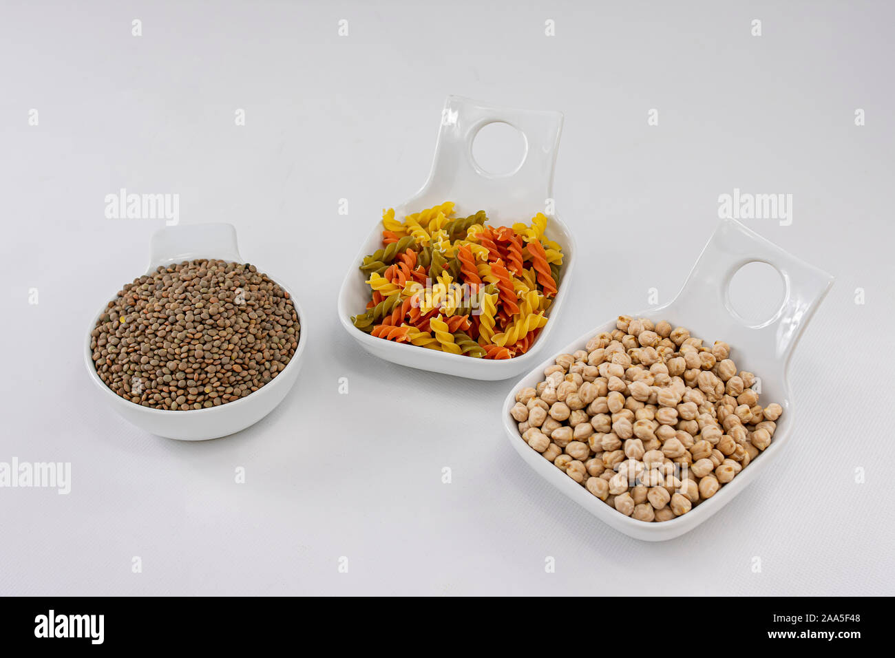 Tre bianchi ciotole con legumi come lenticchie e ceci e pasta con verdure colorate Foto Stock
