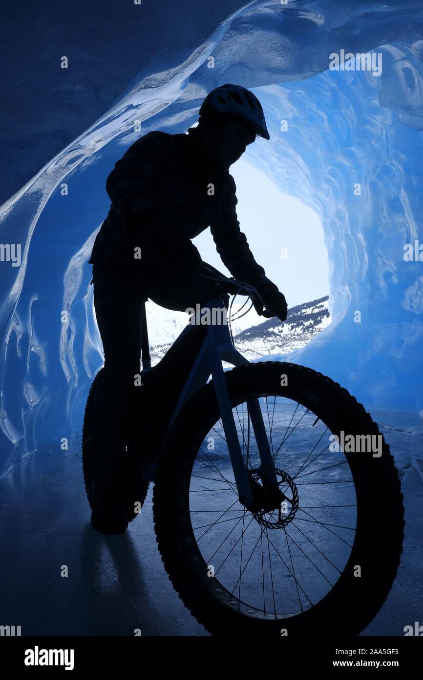 Uomo a cavallo di un fat tire snow bike all'interno di una caverna di ghiaccio in un ghiacciaio in Alaska. Foto Stock
