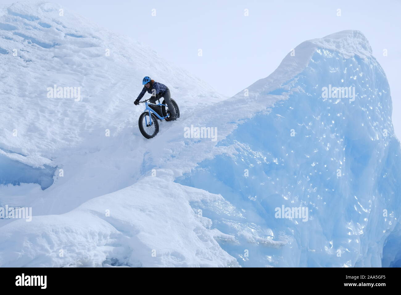 Uomo a cavallo di un fat tire snow bike downhill sulla superficie di un ghiacciaio in Alaska. Foto Stock