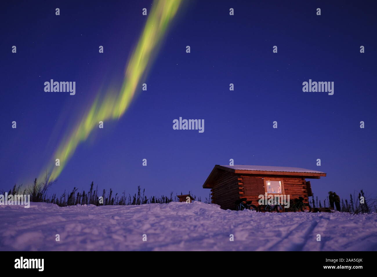 Fat Tire snow bike parcheggiata di fronte una cabina nelle White Mountains, con l'aurora boreale nel cielo. Vicino a Fairbanks Alaska. Foto Stock