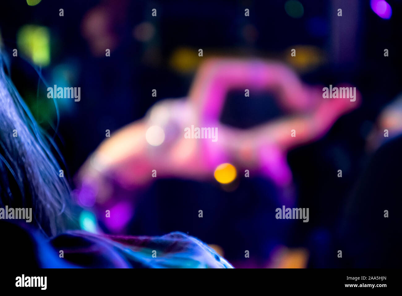 Un dolcemente sfocate, bellissima femmina una danzatrice del ventre con un reggiseno sequined appoggia la schiena con le braccia alzate come ella è guardato dal pubblico in una stanza buia Foto Stock