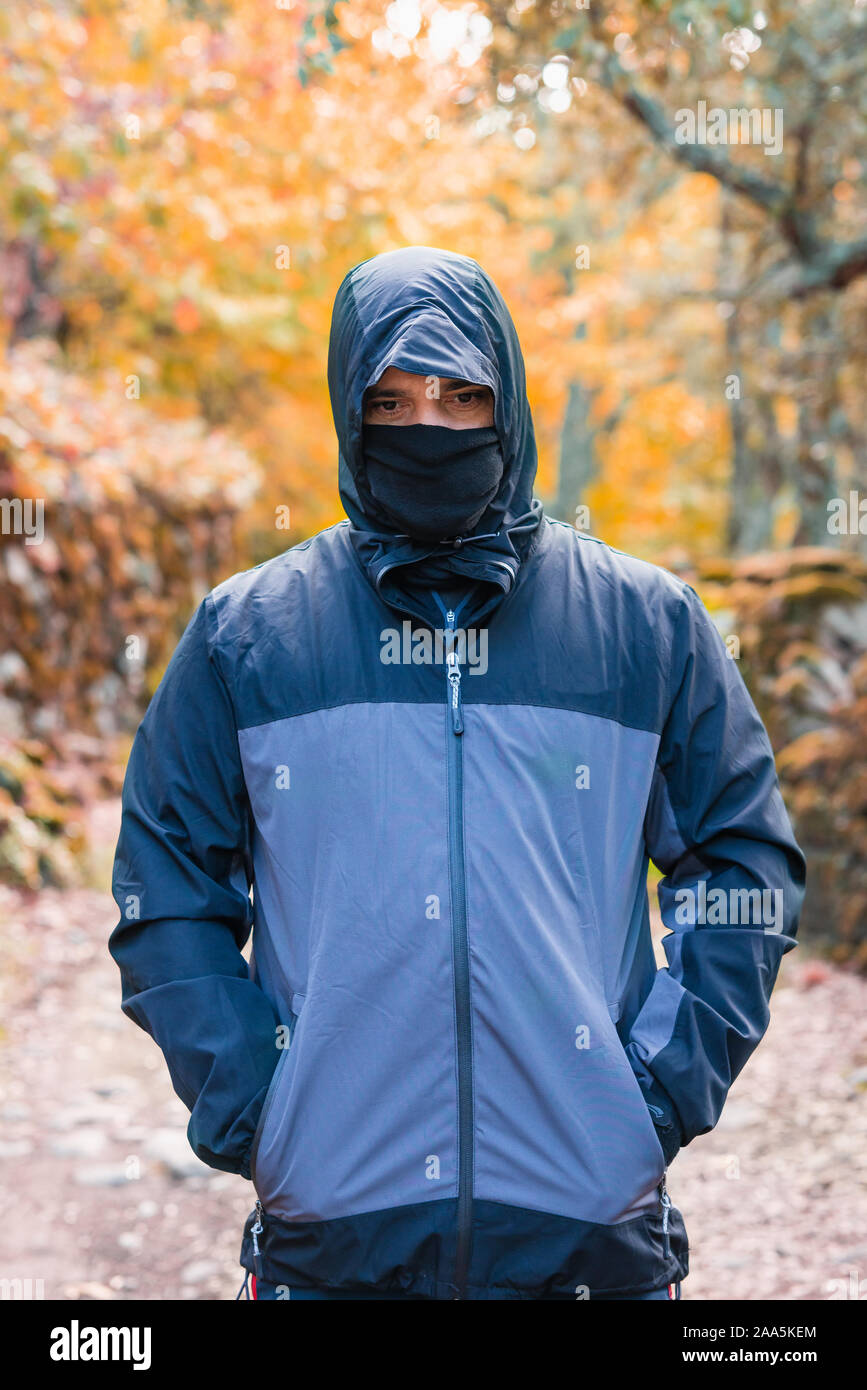 Ritratto di uomo maturo e con felpa con cappuccio e sciarpa sulla bocca della foresta Foto Stock
