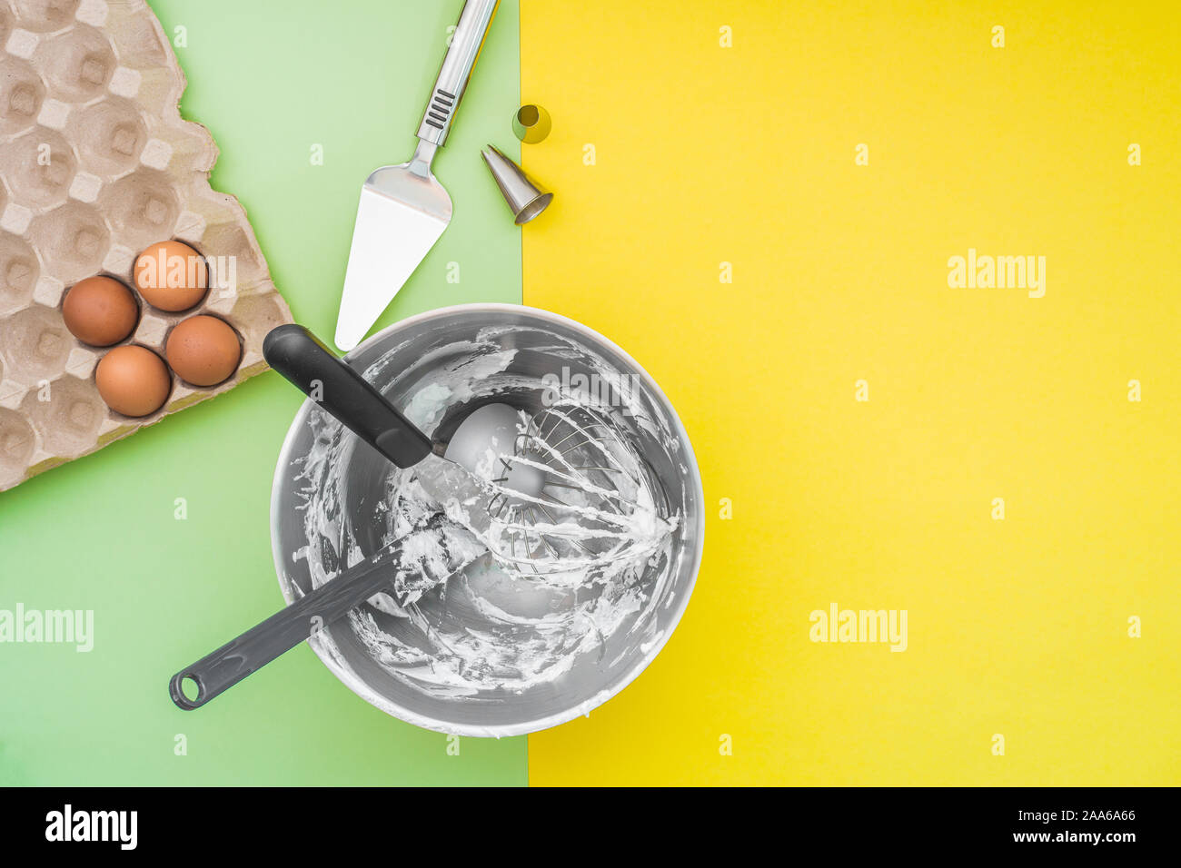 Cottura torte utensili nel recipiente di miscelazione dopo la torta facendo, ugelli, uova crude sul piatto verde laici sfondo giallo Foto Stock