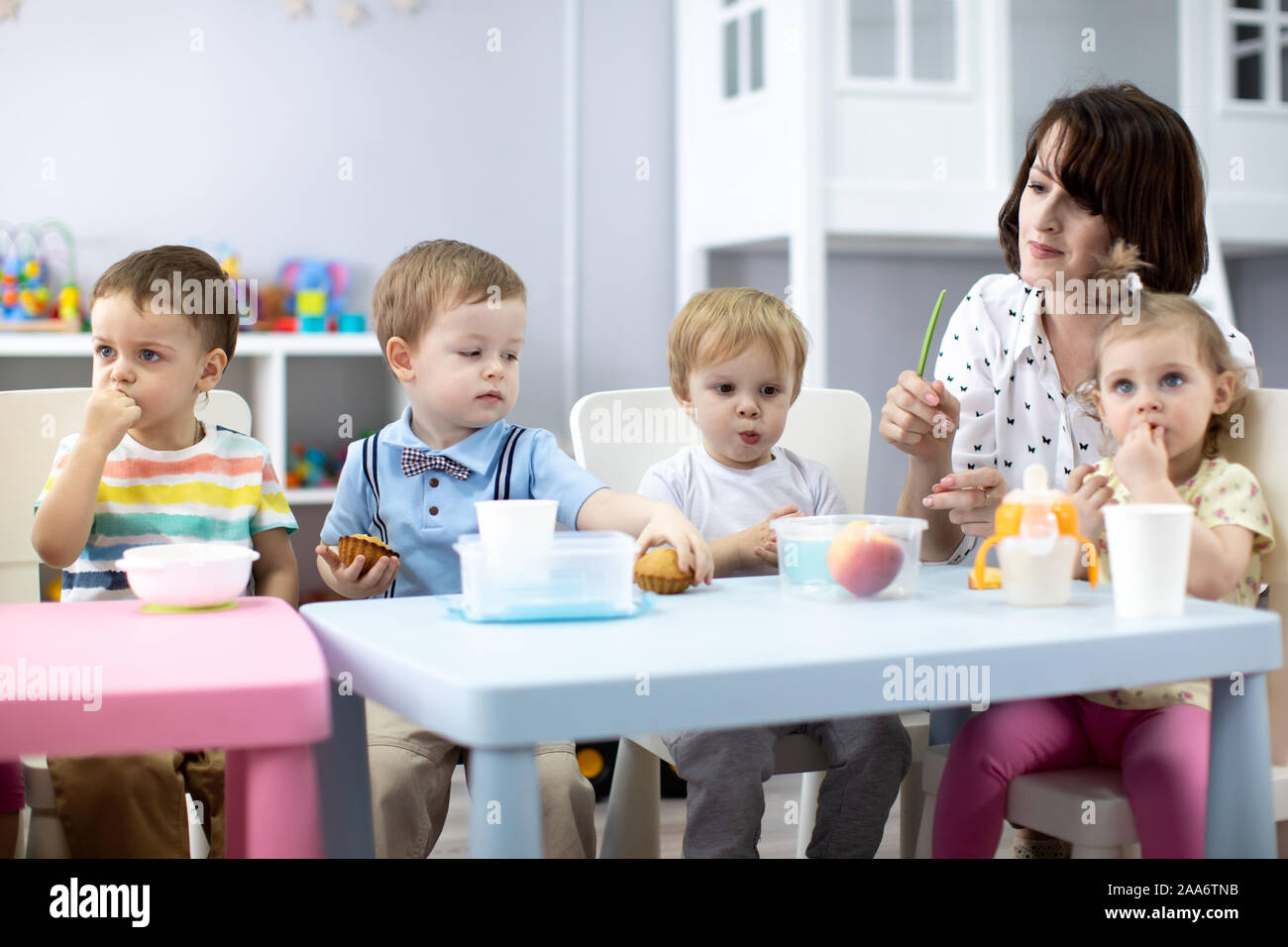 Gruppo di bambini hanno il pranzo con l'insegnante in vivaio. I bambini mangiano cibo da pranzo scatole in kindergarten Foto Stock