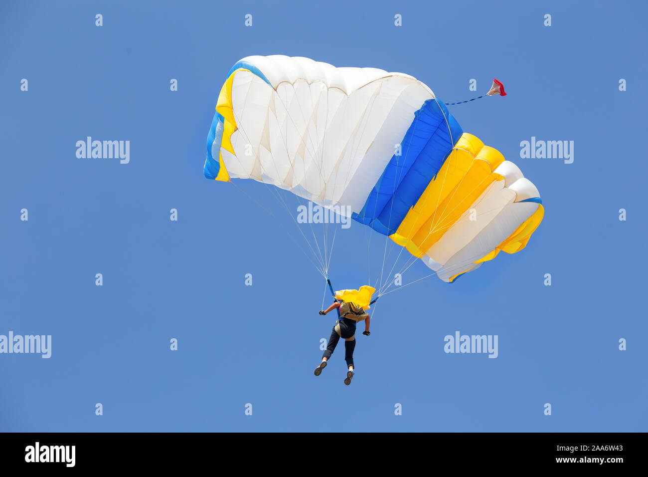 Paracadutista sotto la tettoia di giallo con paracadute blu in un cielo privo di nuvole Foto Stock