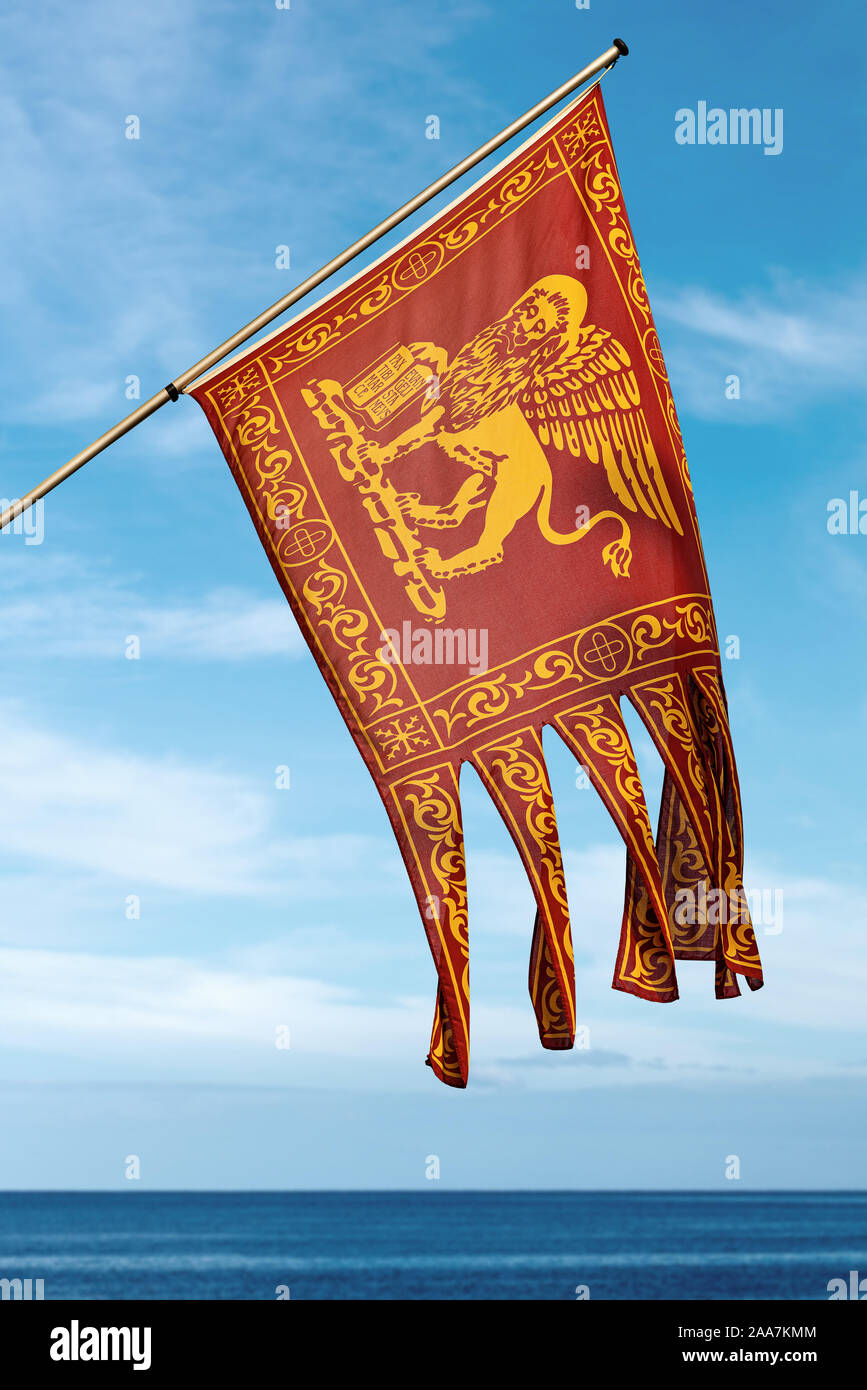 Close-up di una bandiera della città di Venezia e del Veneto con il leone alato di San Marc (San Marco) su un cielo blu con nuvole e mare. Italia Foto Stock