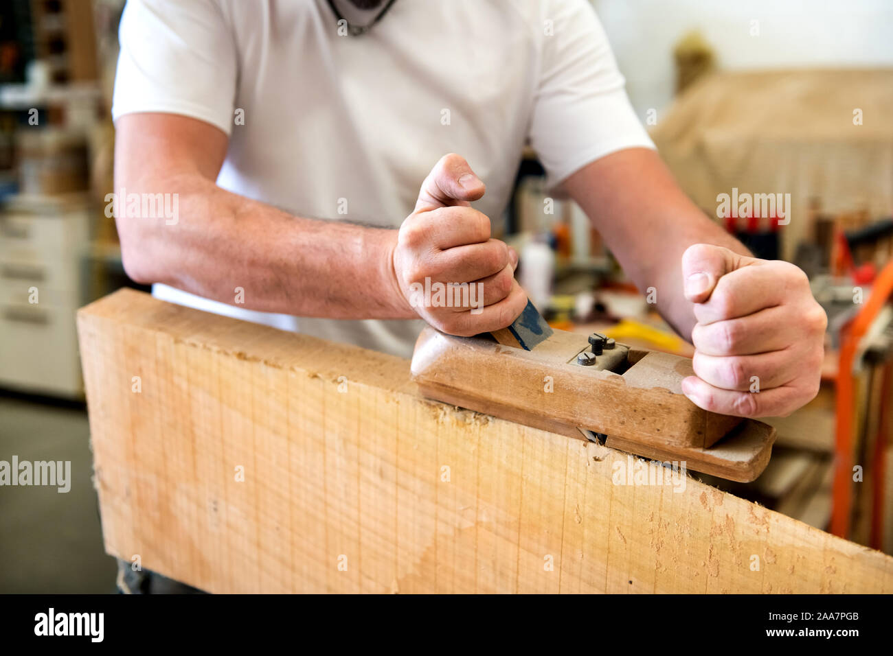 Falegname piallatura la superficie di un pannello di legno con un manuale di piano in una vista ravvicinata nelle sue mani e lo strumento Foto Stock