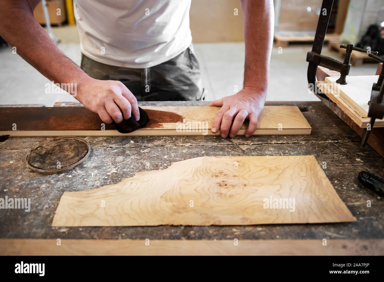 Carpenter applicando macchia di legno per un radiche pannello su un banco di lavoro in un laboratorio di falegnameria in un basso angolo di visione delle sue mani come lavora Foto Stock