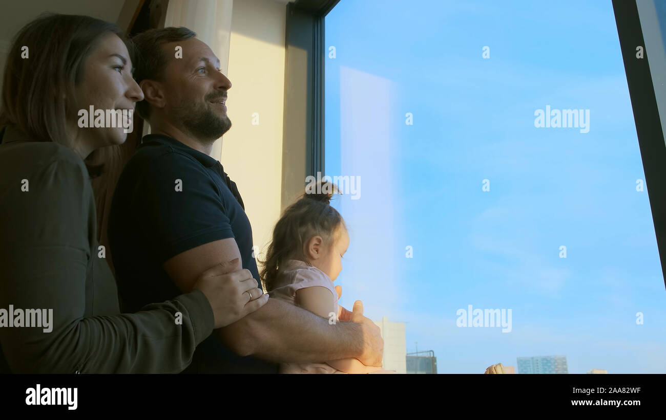 La famiglia è arrivata nella camera di albergo in vacanza. Essi guardano da una finestra a un bellissimo paesaggio urbano Foto Stock