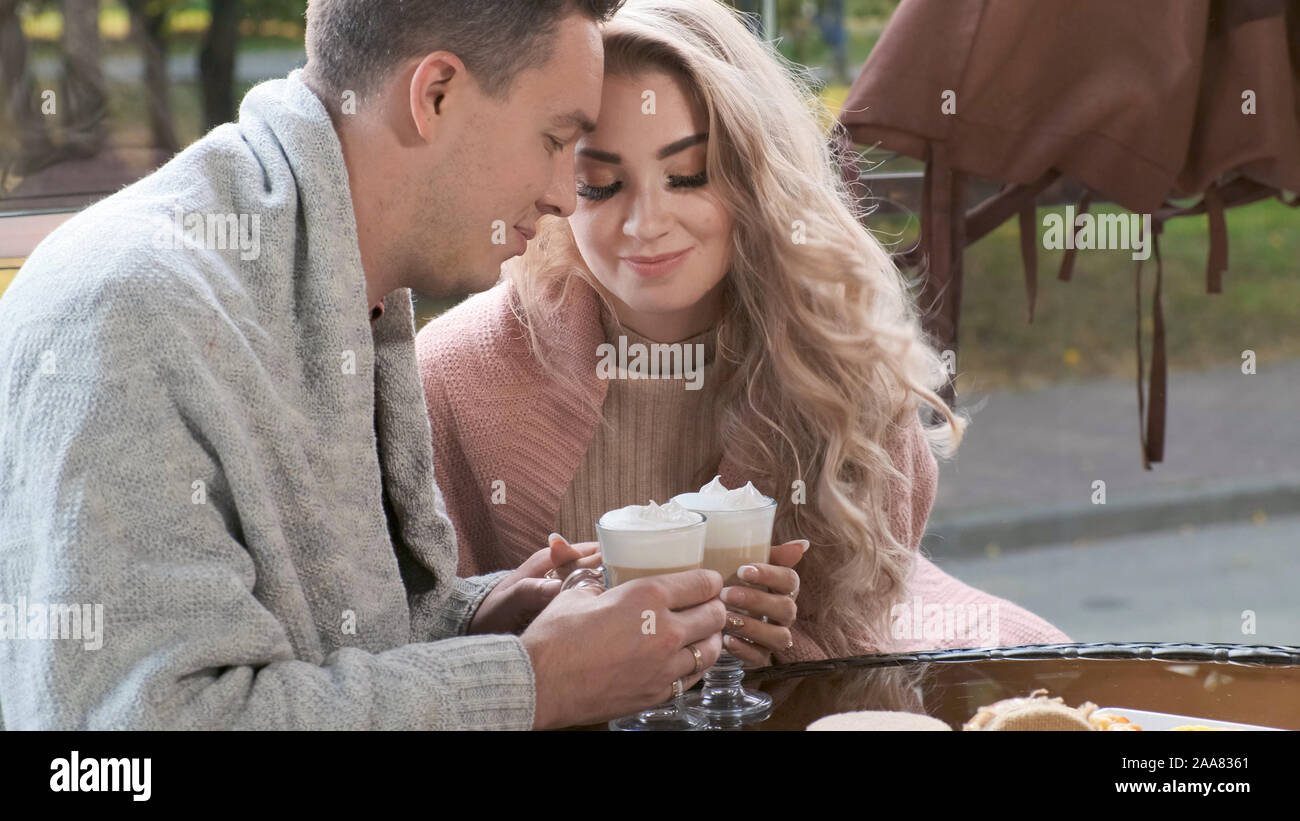 Matura in un bar sulla terrazza. Le mani gli amanti di un uomo e di una donna tenere tazze con cappuccino e latte Foto Stock