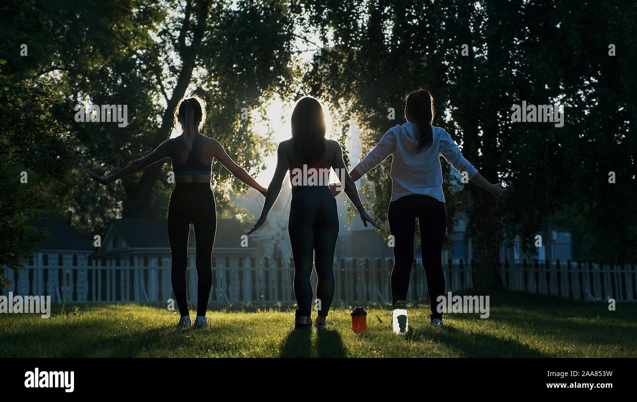 Yoga in aria fresca all'alba. Sagome di tre ragazze amici eseguire esercizi Foto Stock