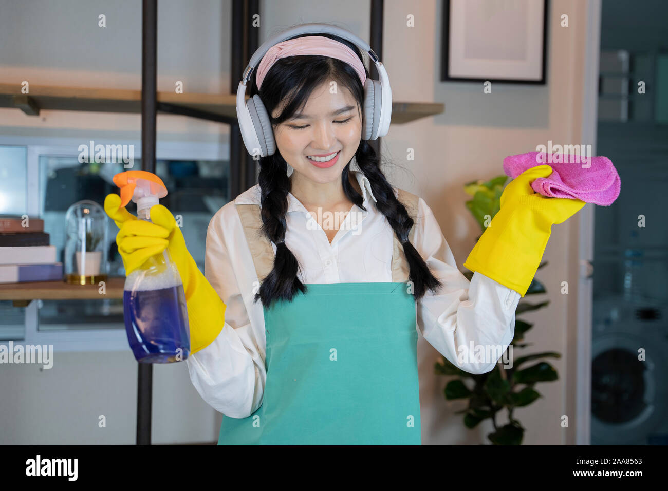 Asian cameriera che si sta godendo le cuffie durante la pulizia della casa  Foto stock - Alamy
