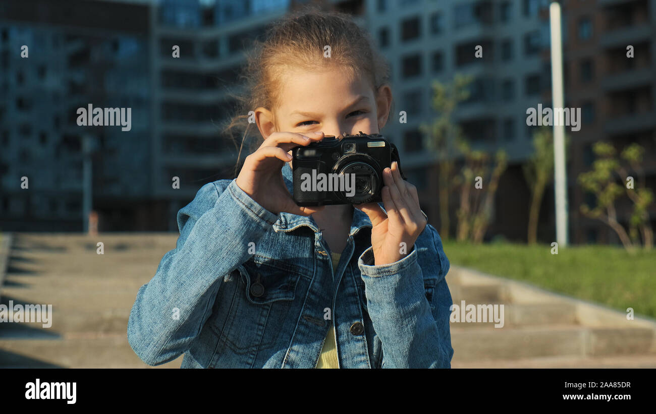 Ritratto di una bambina tenendo una telecamera nelle sue mani. Essa prende le immagini e sorrisi, guarda la telecamera. Foto Stock