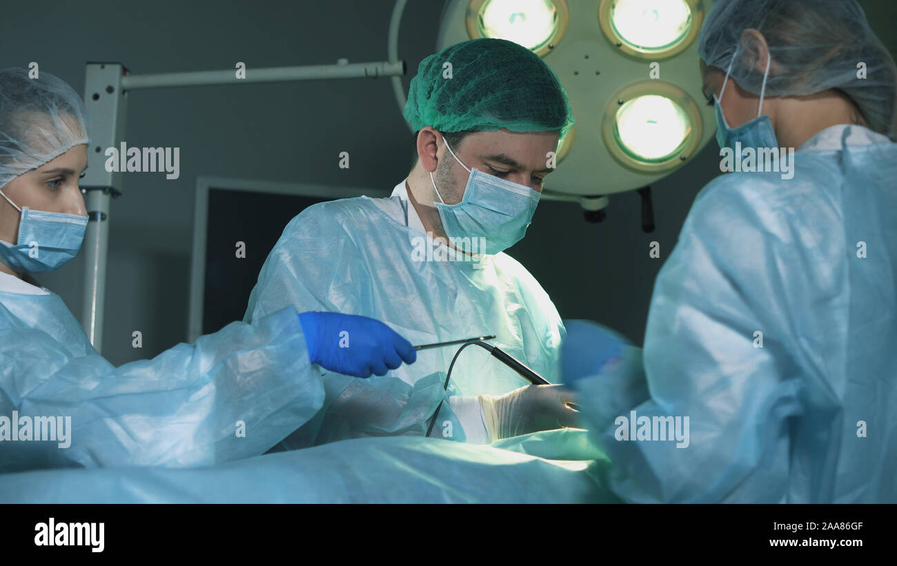 Gruppo di chirurghi al lavoro. L'infermiera dà al medico un medico di clip. Foto Stock