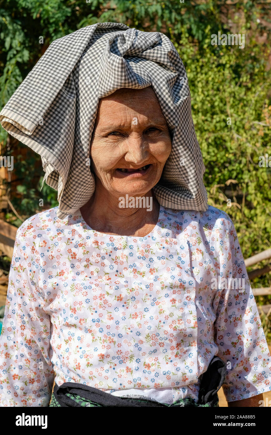 Gli anziani del villaggio birmano donna sorride un sorriso priva di denti e indossa una stoffa tradizionale headdres in un villaggio vicino a Bagan, Myanmar (Birmania) Foto Stock